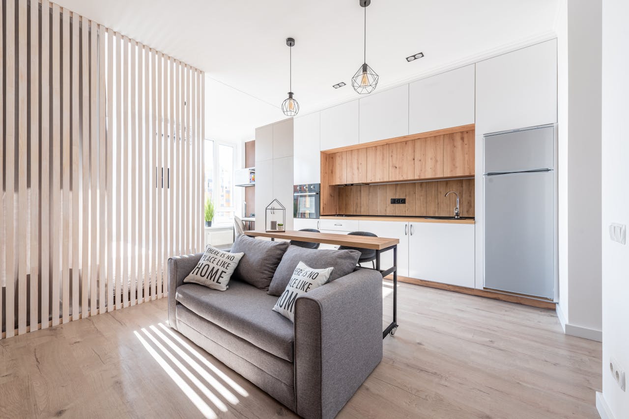 our-services-1 Interior of contemporary open plan kitchen with white cabinets and cozy sofa with cushions in sunlight
