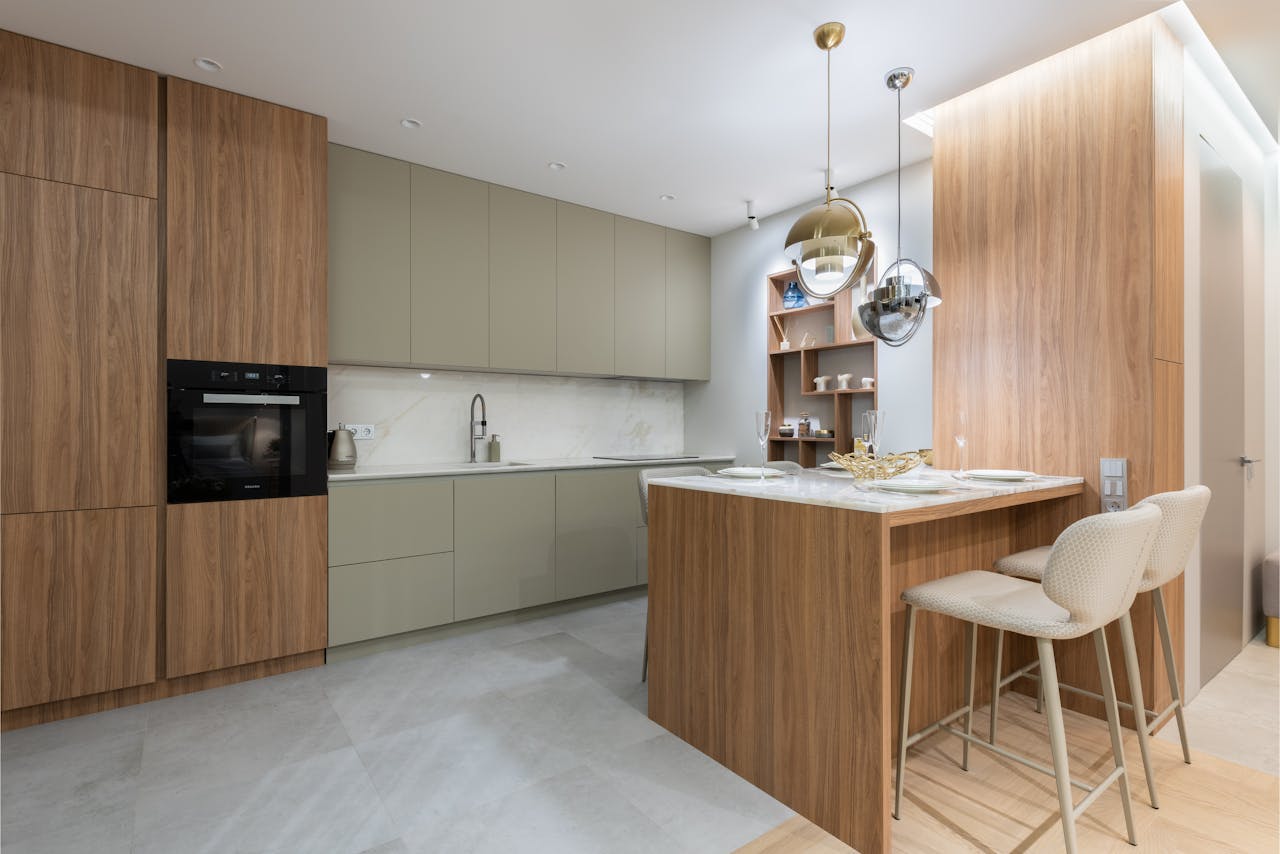 services-02 Interior of bright modern kitchen with cupboards near chairs with counter decorated with glasses and plates under lamps next to shelves on wall