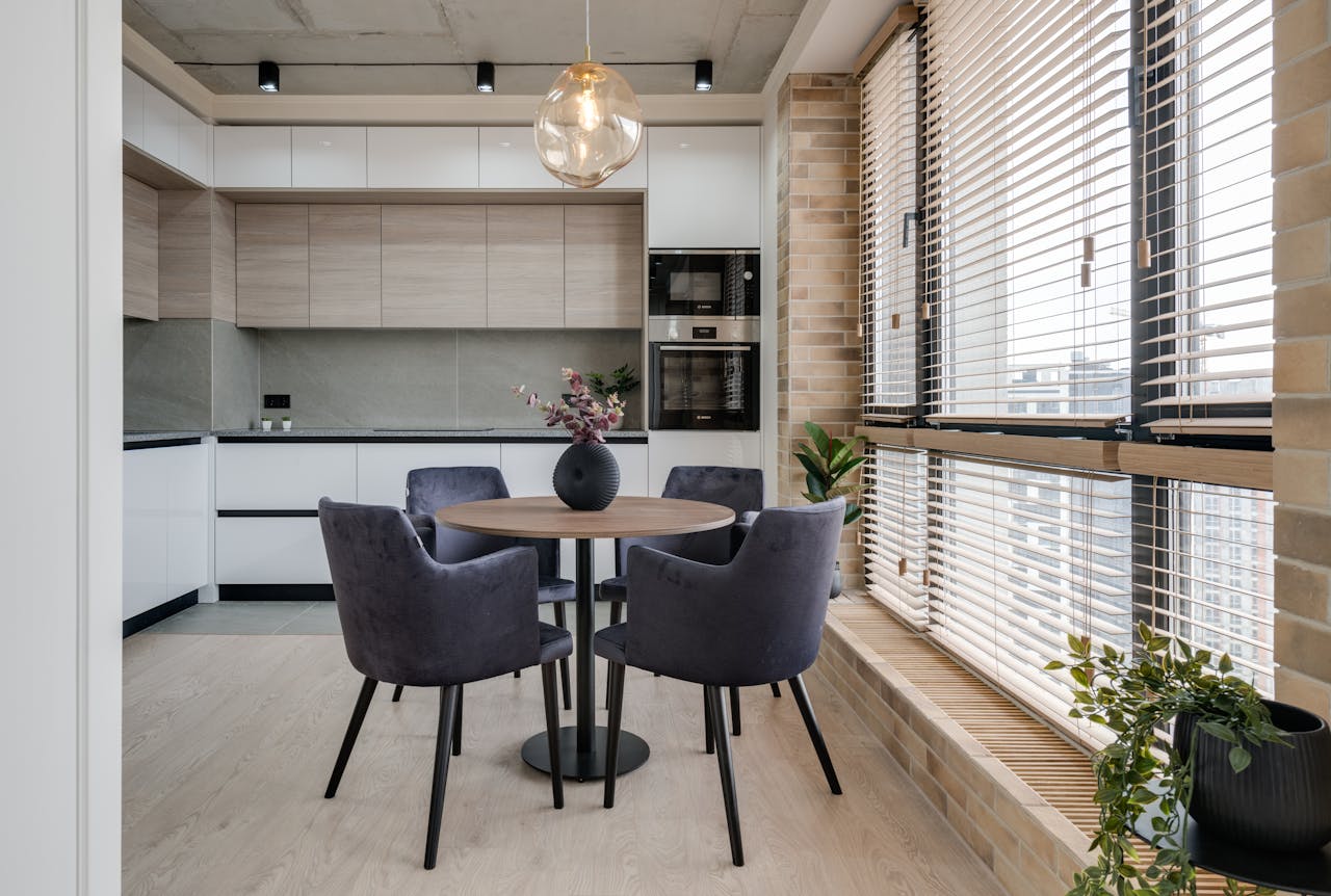 our-services-3 Spacious minimalist kitchen with round table and elegant chairs by large windows, perfect for bright spaces.